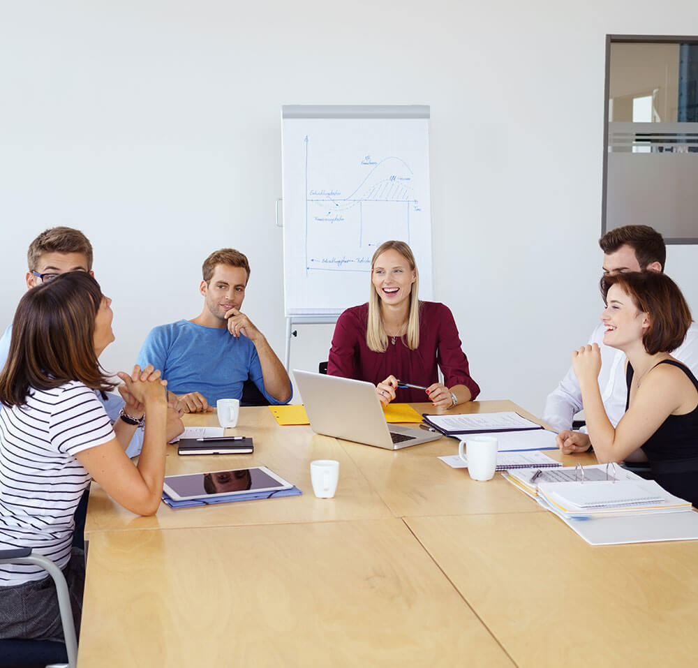 Mehrere junge Menschen sitzen um einen Tisch und unterhalten sich angeregt