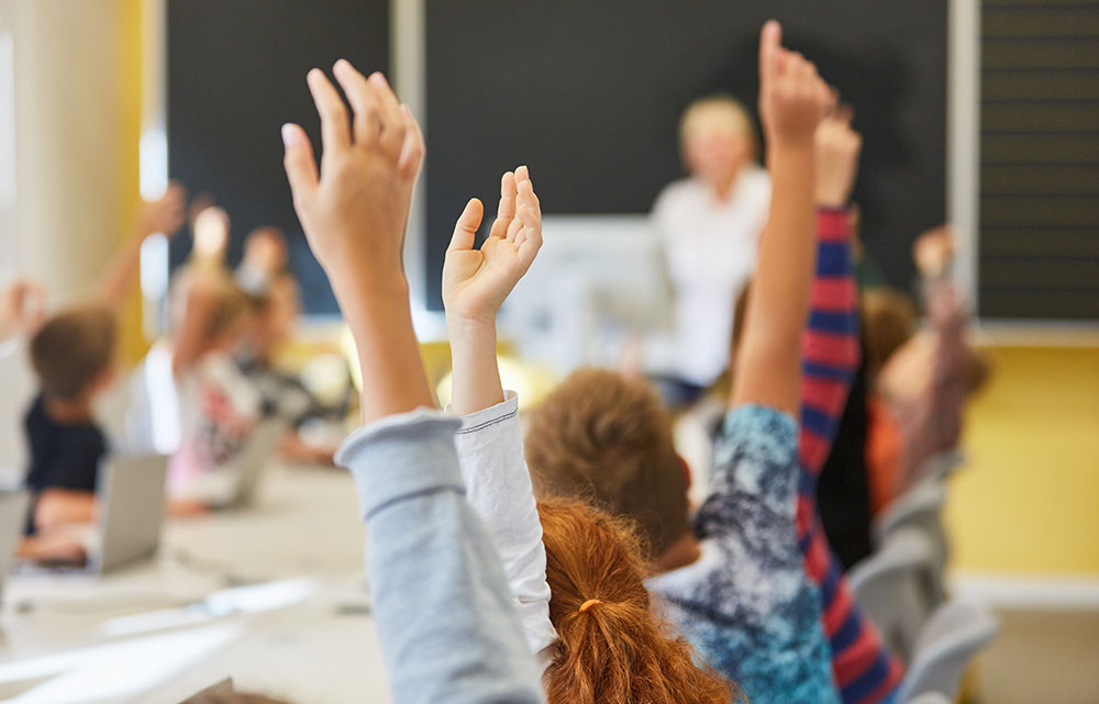 Erhobene Kinderhände in einer Schulklasse