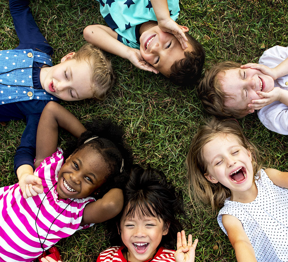 Lachende Kinder liegen im Kreis auf einer Wiese